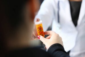 Female medicine doctor hand hold jar of pills and write prescription to patient at worktable. Panacea and life save prescribing treatment legal drug store concept.